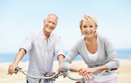 retired couple riding bikes on the beach enjoying life